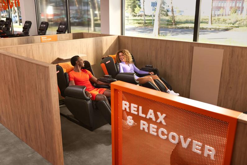 Man and woman chatting while using massage chairs at Basic-Fit.